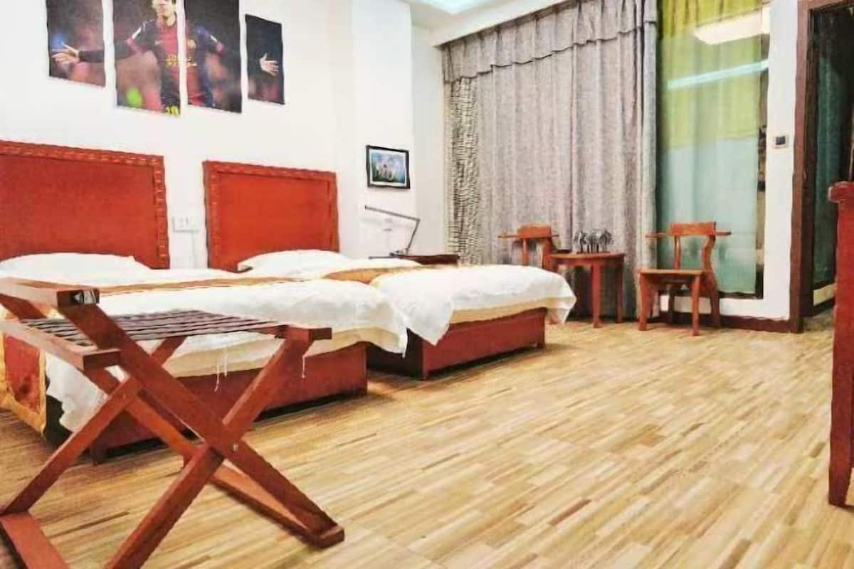 Een hotelkamer met twee bedden, een houten vloer, een raam met gordijnen en een kleine tafel met stoelen.
