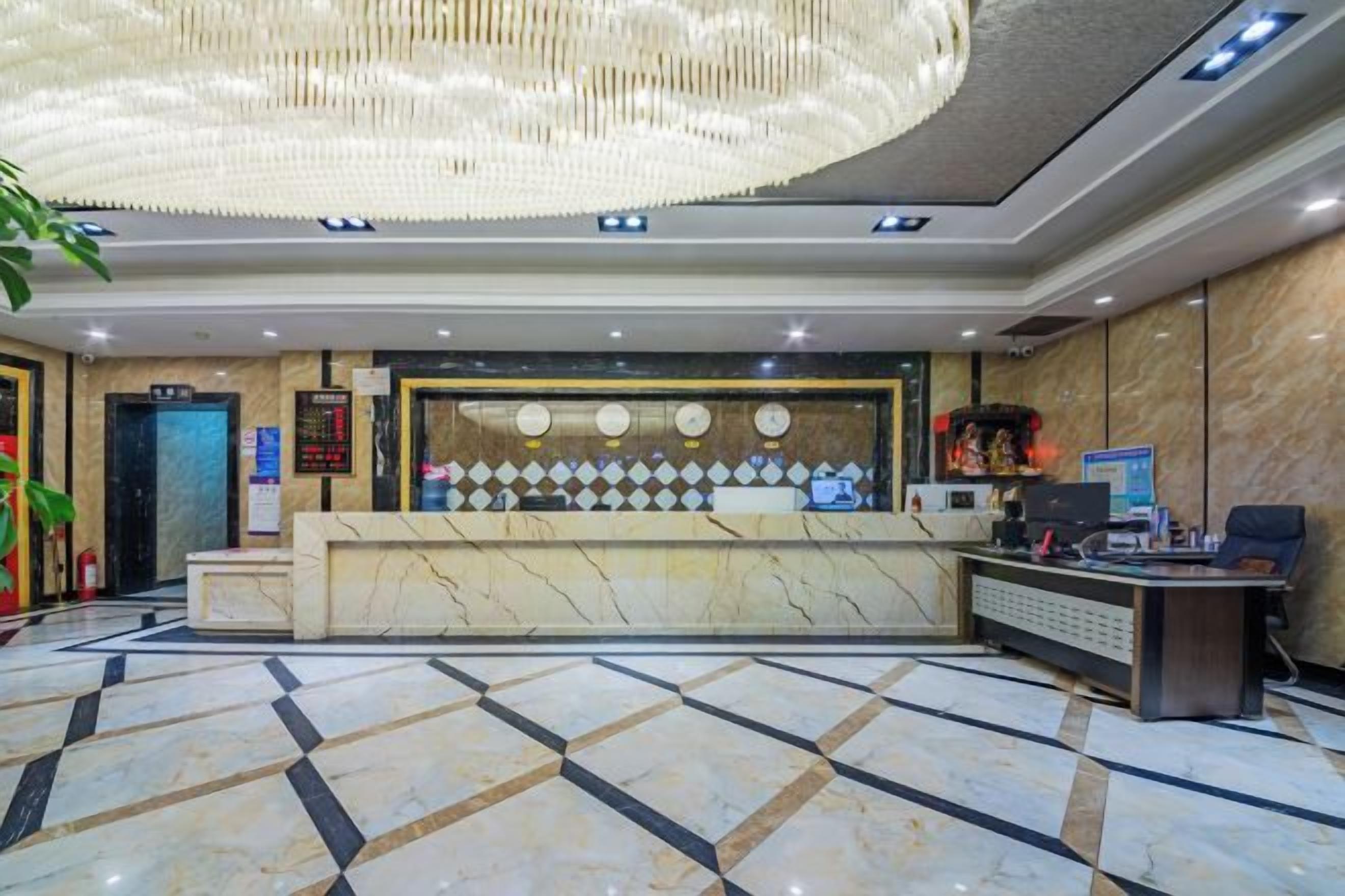 Área de recepção de hotel com balcão de mármore, um candelabro e um painel digital.