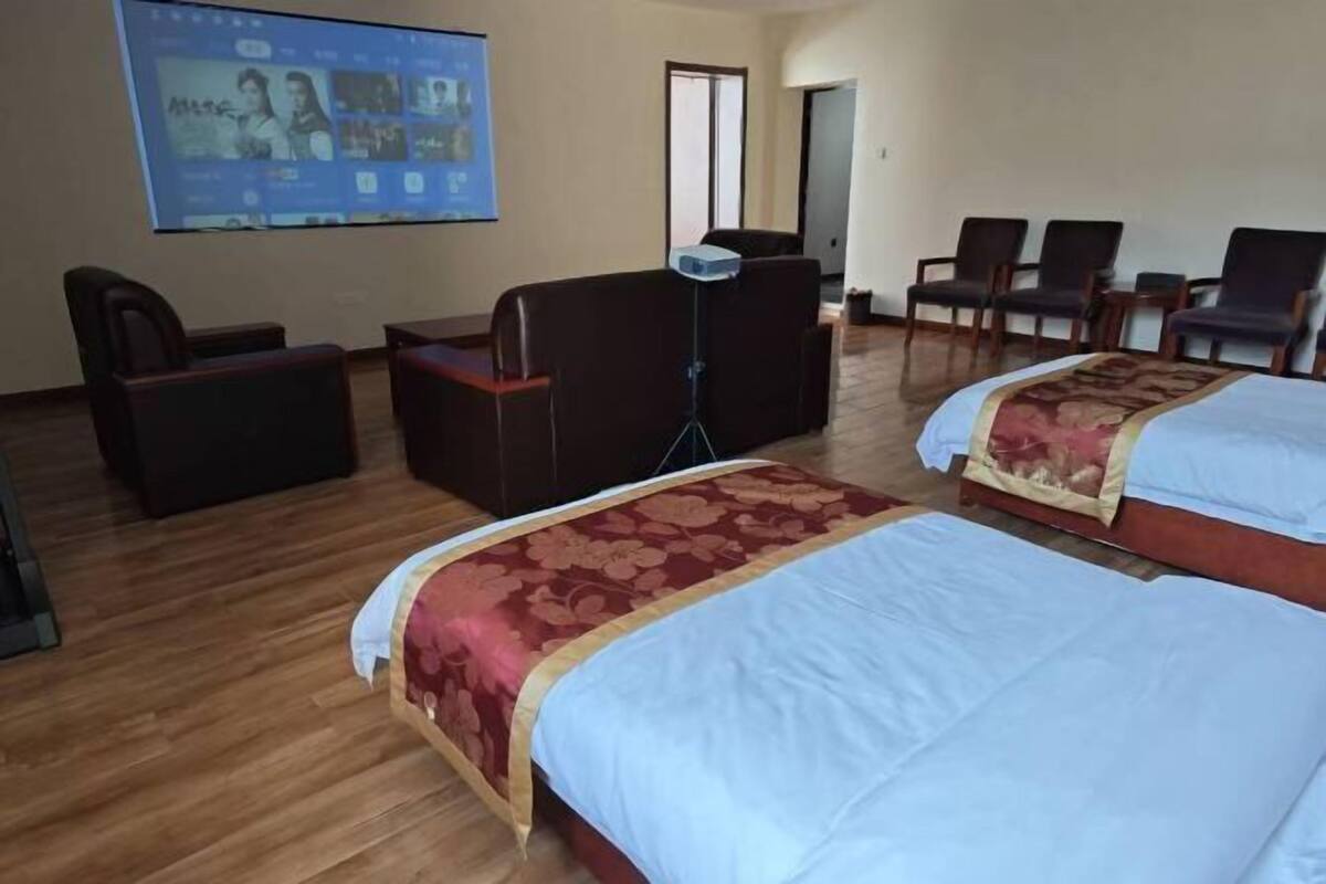 Een hotelkamer met twee bedden, een bureau, een stoel en een televisiescherm waarop een film wordt afgespeeld.