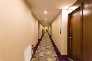 A hotel hallway with a patterned carpet, wooden doors, and a fire extinguisher on the wall. - Lanzhou Huayu Business Hotel (Lanzhou)