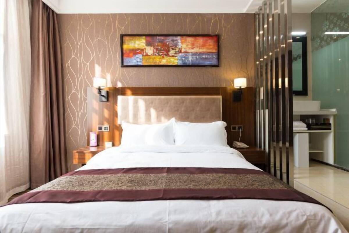 Een hotelkamer met een groot bed, een hoofdeinde, een nachtkastje met een lamp en een schilderij aan de muur.