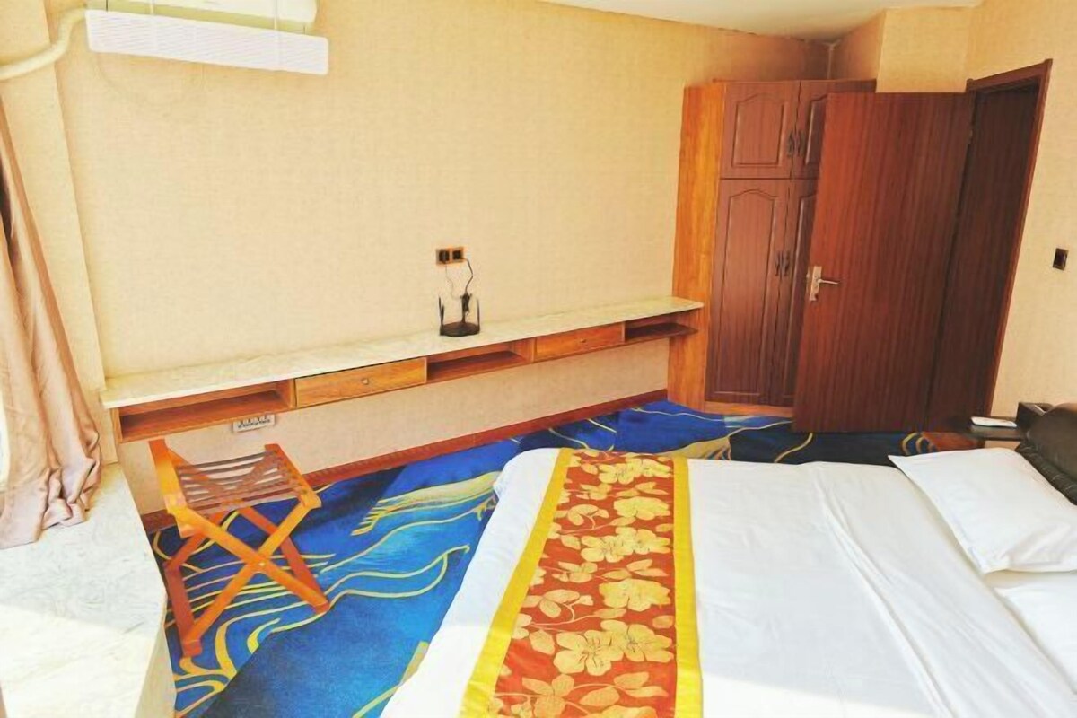 Habitació d'hotel amb un llit, un armari de fusta, un escriptori amb una cadira i una petita taula amb una làmpada.