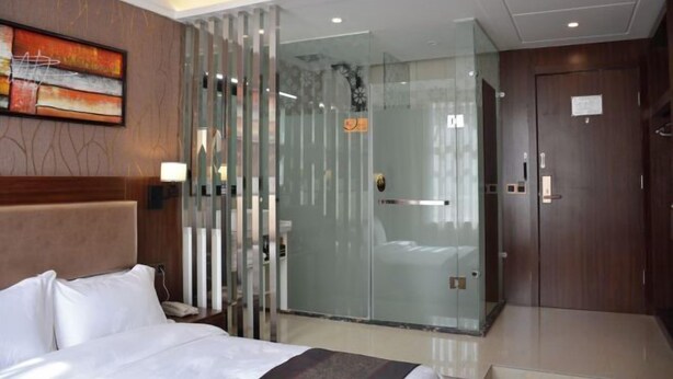 Habitación de hotel con cama, un separador de vidrio, una puerta de madera y una obra de arte colgada en la pared.