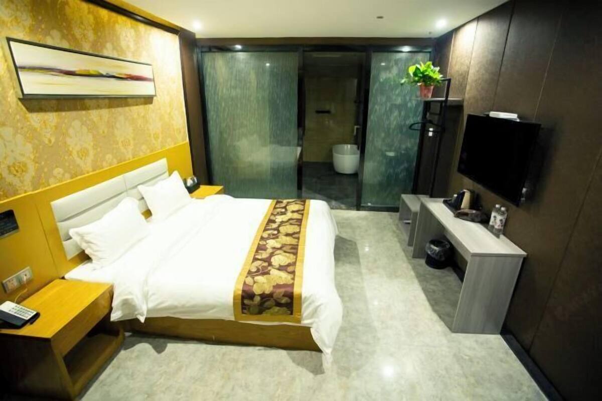 Een moderne hotelkamer met een bed, nachtkastje, televisie en een badkamer zichtbaar door een glazen deur.