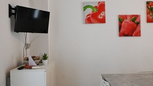 Ein Zimmer mit flachbildfernseher an der Wand, einer kleinen Speisekammer mit Snacks, einer Topfpflanze und einem Esstisch mit Stuhl.