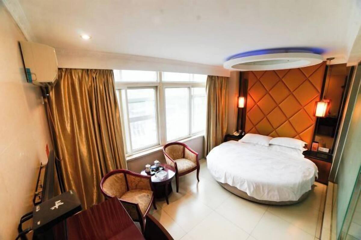 Habitación de hotel con una cama grande, un escritorio con silla, una mesita y una ventana con cortinas.