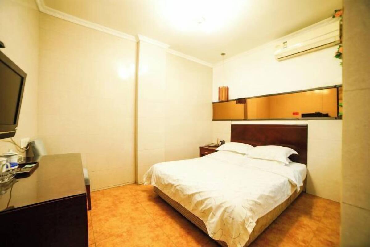 Habitación de hotel con cama, escritorio, silla, televisor y estante con objetos decorativos.