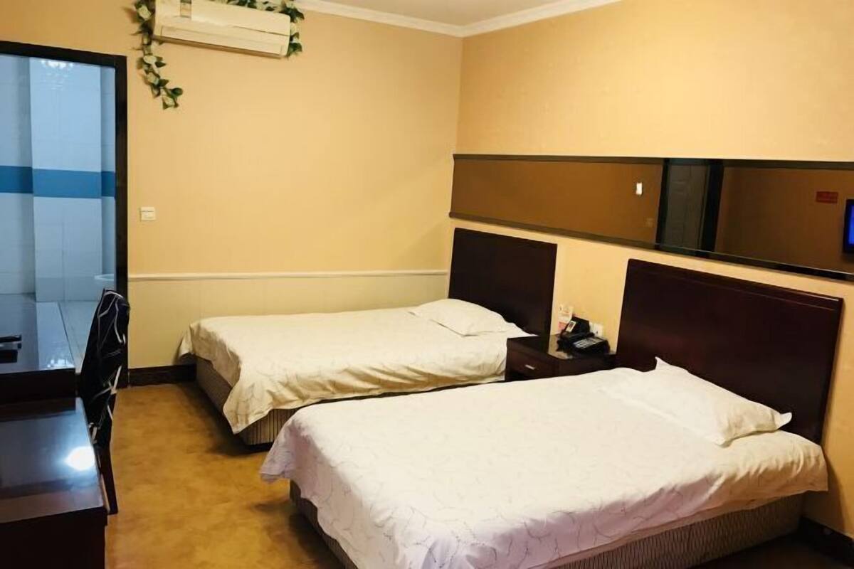 Habitación de hotel con dos camas individuales, un escritorio, una silla, un televisor y un espejo en la pared.