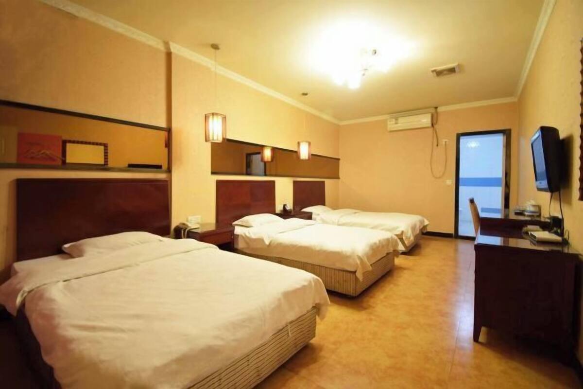 Habitación de hotel con tres camas individuales, un escritorio con silla, televisión y puerta que da a un balcón.