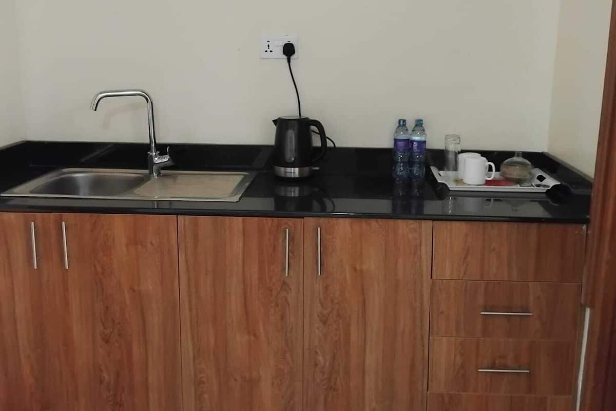 A small kitchenette with a sink, a kettle, and a coffee maker. There are two bottles of water and a white mug on the counter.