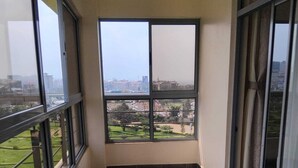 Un balcón con amplias ventanas que ofrece vistas a un paisaje urbano y zonas verdes.