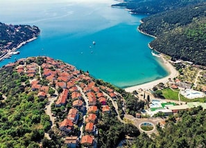 An aerial view of a coastal town with a cluster of red-roofed buildings, a beach, and a marina. - 2-bedroom Apartment in Drenje (Rasa)