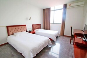 A hotel room with two beds, a desk, a chair, an air conditioning unit, and a window with curtains.