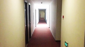 Un pasillo estrecho y alfombrado con puertas a ambos lados, que conduce a una habitación luminosa al final.