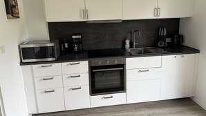 Cozinha moderna com armários brancos, micro-ondas, cafeteira, pia e fogão.