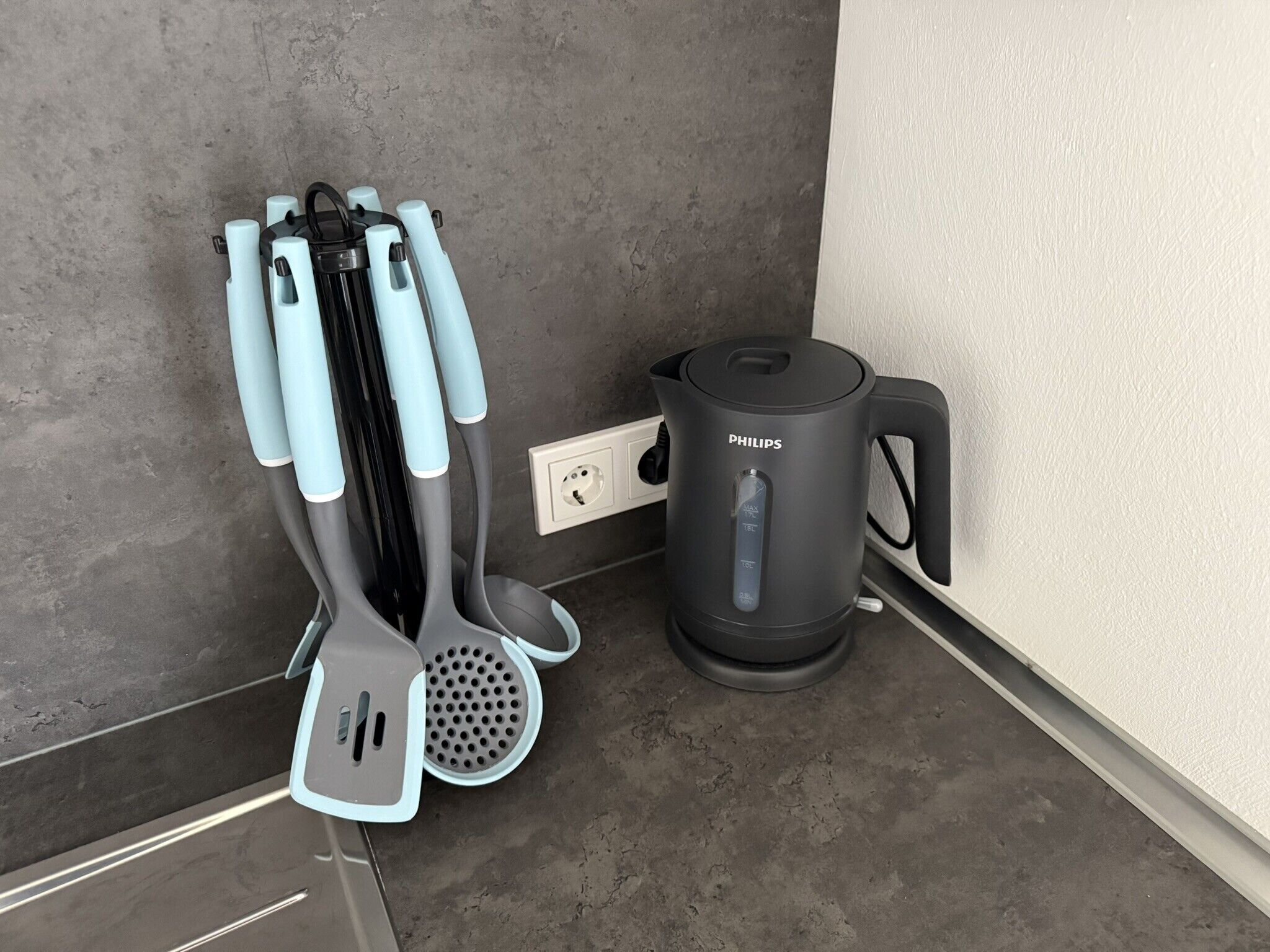A kitchen with a black Philips electric kettle, a white power outlet, and a set of kitchen utensils with blue handles.