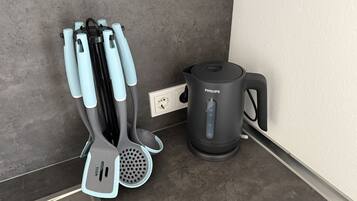 A kitchen with a black Philips electric kettle, a white power outlet, and a set of kitchen utensils with blue handles.