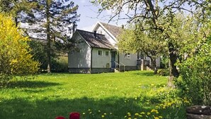 Ett hus med ett sluttande tak, omgivet av en gräsyta och träd.