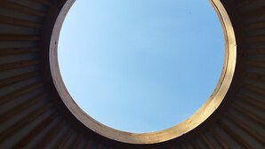 A circular skylight with a wooden frame and a clear blue sky visible through it.
