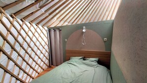 A small, enclosed sleeping area with a wooden frame, a single bed with green bedding, and a curtain.