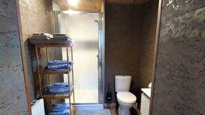 A compact bathroom with a shower, toilet, and a shelf with folded towels.