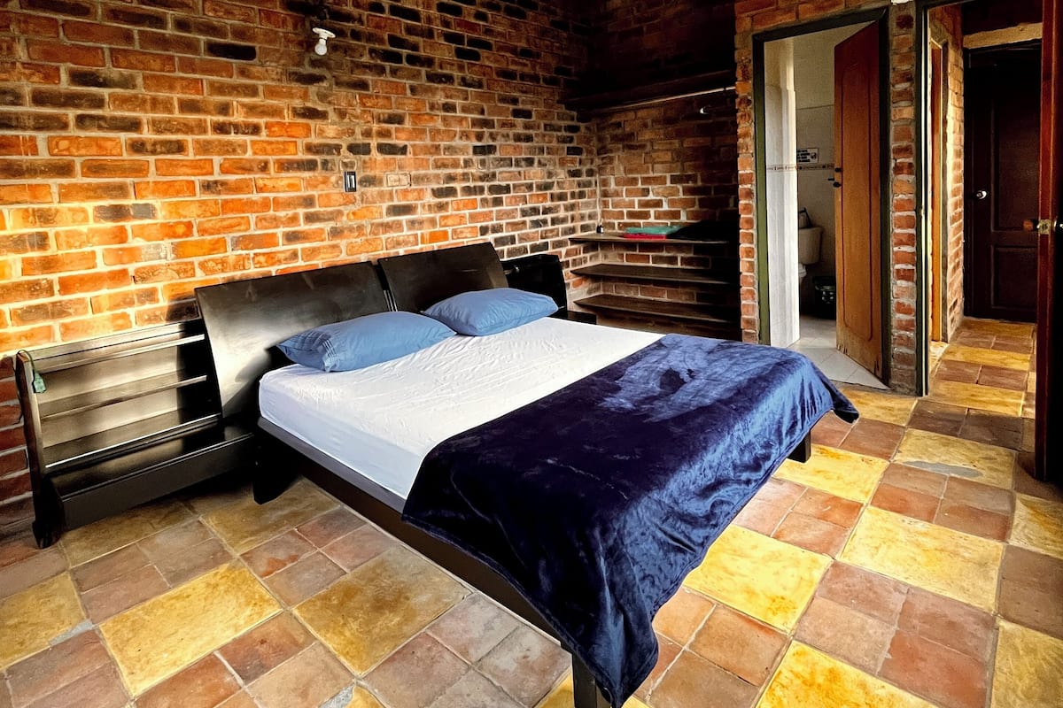 Un dormitorio con pared de ladrillo, techo de madera y cama con colcha azul.