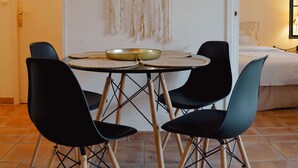 Un comedor con una mesa redonda y cuatro sillas, un atrapasueños colgado en la pared, y una cama en la habitación contigua.