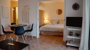 Habitación de hotel con cama, televisión, zona de comedor con sillas y un reloj en la pared.