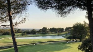 Un campo de golf con un estanque, árboles y cielo despejado.