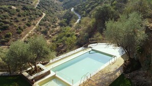 A rectangular swimming pool with a wooden deck and stone borders, surrounded by greenery and overlooking a valley with a winding road. - Bairro do Casal turismo rural (Vila Nova de Foz Côa)
