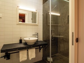 Un baño con lavamanos blanco, un espejo y cabina de ducha con mampara de vidrio.