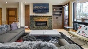 Una sala de estar moderna con chimenea, un sofá, una mesa de centro y vistas al exterior.