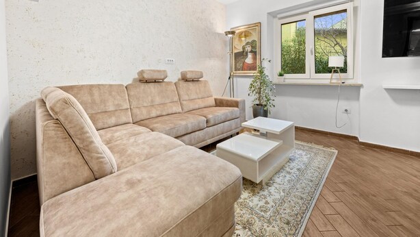 A modern living room with a beige sectional sofa, a white coffee table, and a large window with a view of greenery.