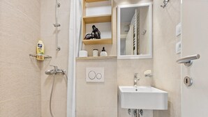 A modern bathroom with a shower, toilet, sink, and storage shelves.