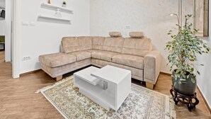 A modern living room with a beige sectional sofa, a white coffee table, a patterned rug, and a potted plant.