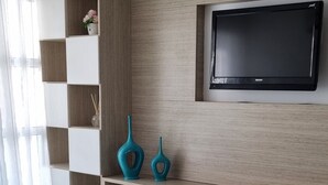 Una sala moderna con un televisor de pantalla plana montado en una pared de madera, un sofá blanco y un mueble empotrado con estanterías.