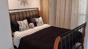 Un dormitorio con cama, un adorno en la pared, una ventana con cortinas e iluminación en el techo.