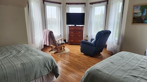 Une chambre avec deux lits, un fauteuil à bascule, une télévision et une commode.