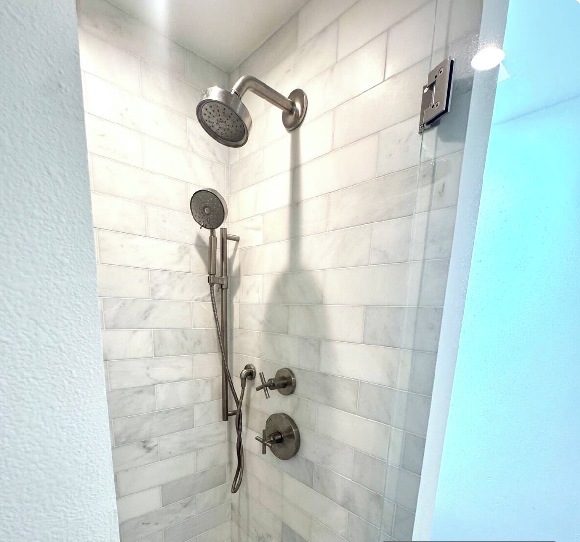 A shower with a handheld showerhead and a wall-mounted faucet.