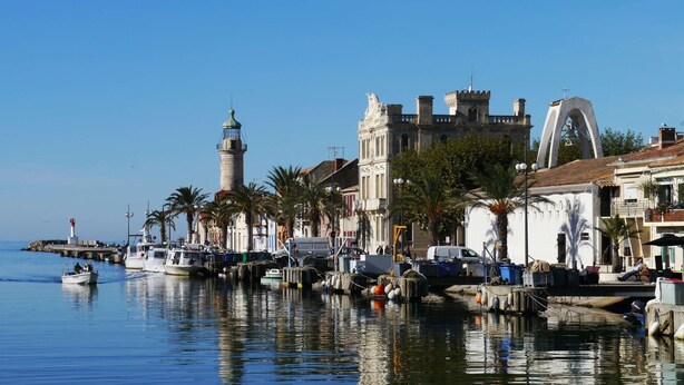 A waterfront with boats docked, a lighthouse, and historic buildings. - Studio cabin terrace swimming pool parking (LE GRAU DU ROI)