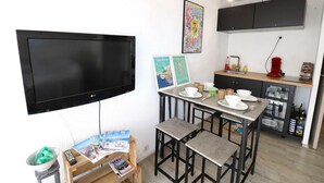 A compact living space with a flat-screen TV, a dining area with stools, a kitchen with cabinets, and a wall-mounted shelf. - Studio cabin terrace swimming pool parking (LE GRAU DU ROI)