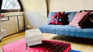 Een gezellige woonkamer met een blauwe bank, een rood gestreept voetenbankje en een boekenkast.