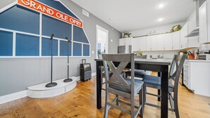 A modern kitchen with white cabinets, a wooden dining table, and a blue accent wall with a 'Grand Ole Opry' sign. - Penthouse Near Grand Ole Opry w/ Private Rooftop + Karaoke Stage + 3BR/3BA (Nashville)