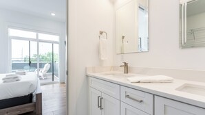 A modern bathroom with a large mirror, a sink, and a toilet. There is a bed with white linens in the adjacent room. - Penthouse Near Grand Ole Opry w/ Private Rooftop + Karaoke Stage + 3BR/3BA (Nashville)