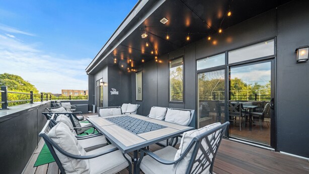 An outdoor deck with a table and chairs, a view of the surrounding area, and a building with large windows. - Penthouse Near Grand Ole Opry w/ Private Rooftop + Karaoke Stage + 3BR/3BA (Nashville)