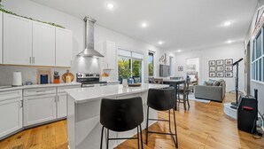 A modern kitchen with white cabinets, a central island, and black bar stools. - Penthouse Near Grand Ole Opry w/ Private Rooftop + Karaoke Stage + 3BR/3BA (Nashville)