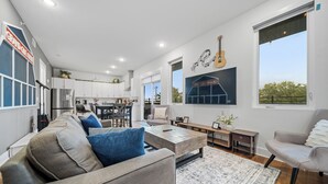 A modern living room with a sofa, coffee table, and a view of the kitchen. - Penthouse Near Grand Ole Opry w/ Private Rooftop + Karaoke Stage + 3BR/3BA (Nashville)