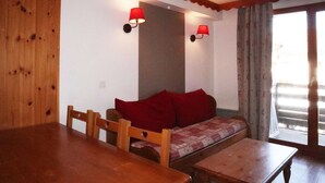 A wooden dining table with chairs, a sofa with red cushions, and two wall-mounted lamps.