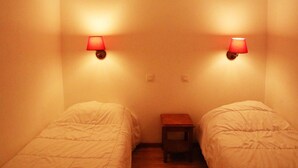A room with two single beds, a small wooden nightstand, and two wall-mounted lamps.