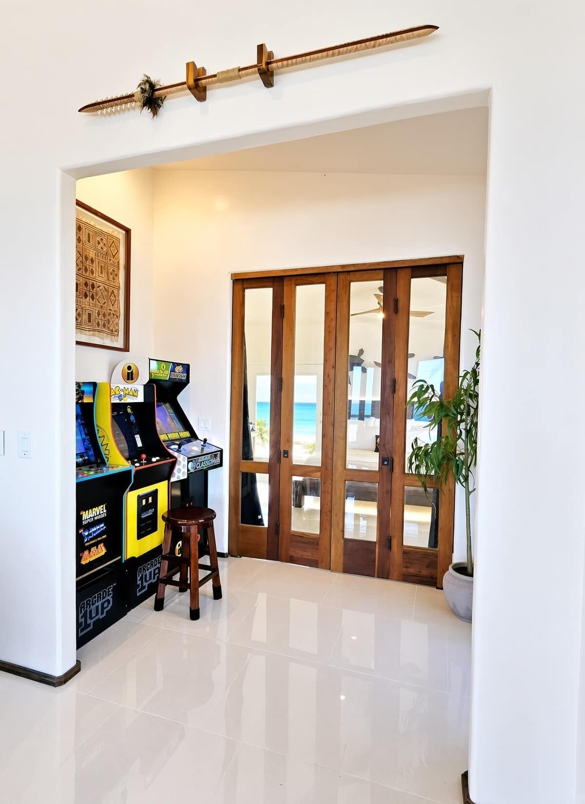 A room with a wooden door leading to a balcony, arcade games, a framed picture, and a potted plant.